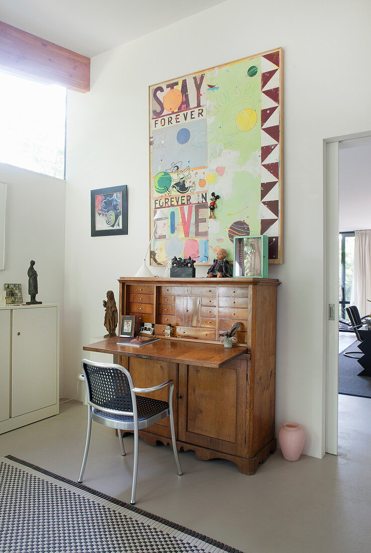 Metal chair at antíque bureau below modern painting