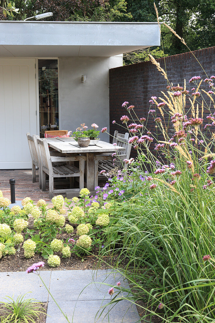 A view over a bed of hydrangeas to a terrace with a wooden table and chairs