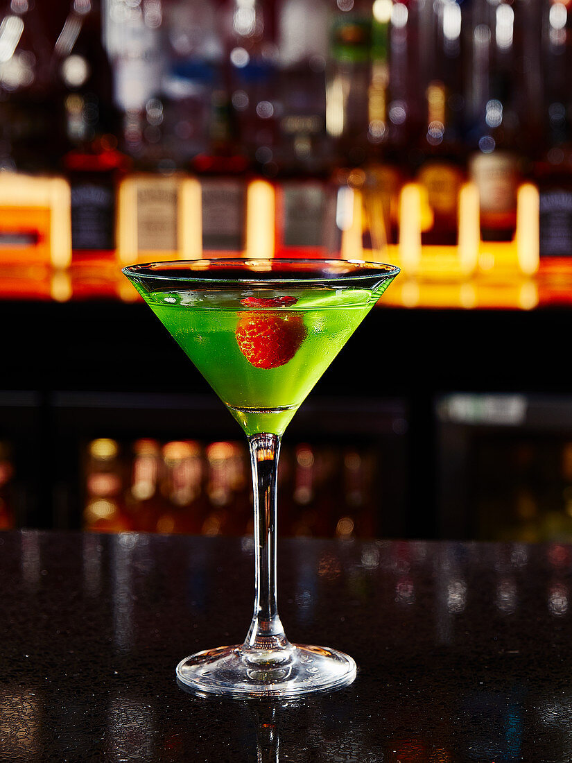 A green cocktail with a raspberry in a bar