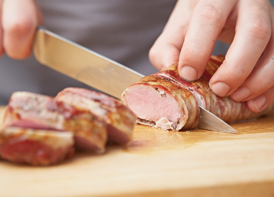Pork fillet wrapped in bacon being sliced