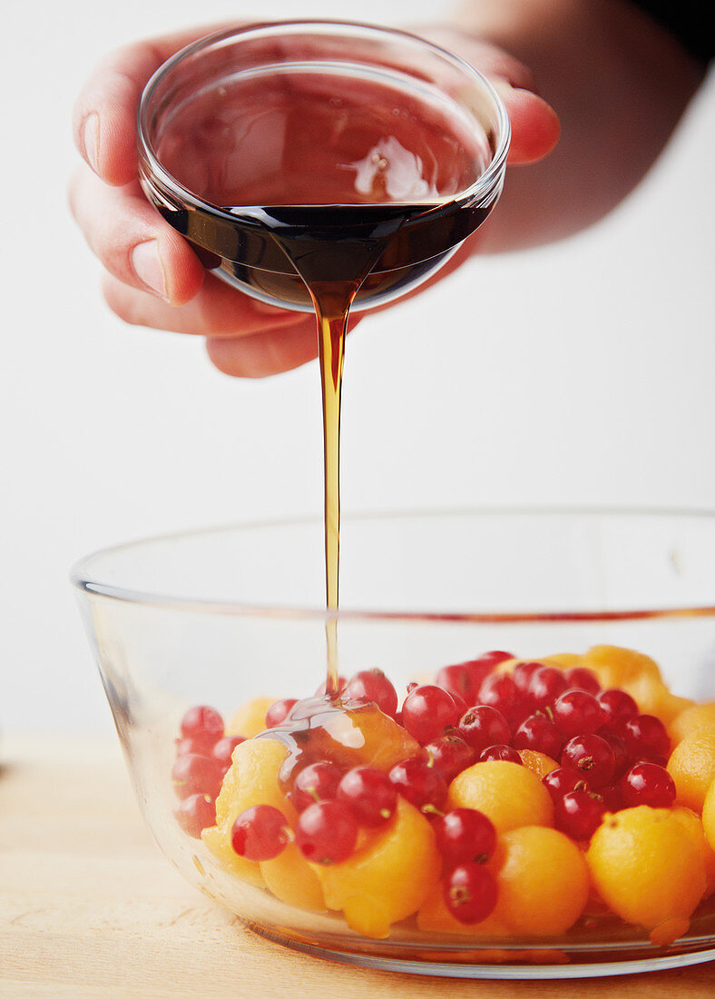 Maple syrup being poured over melon balls and redcurrants