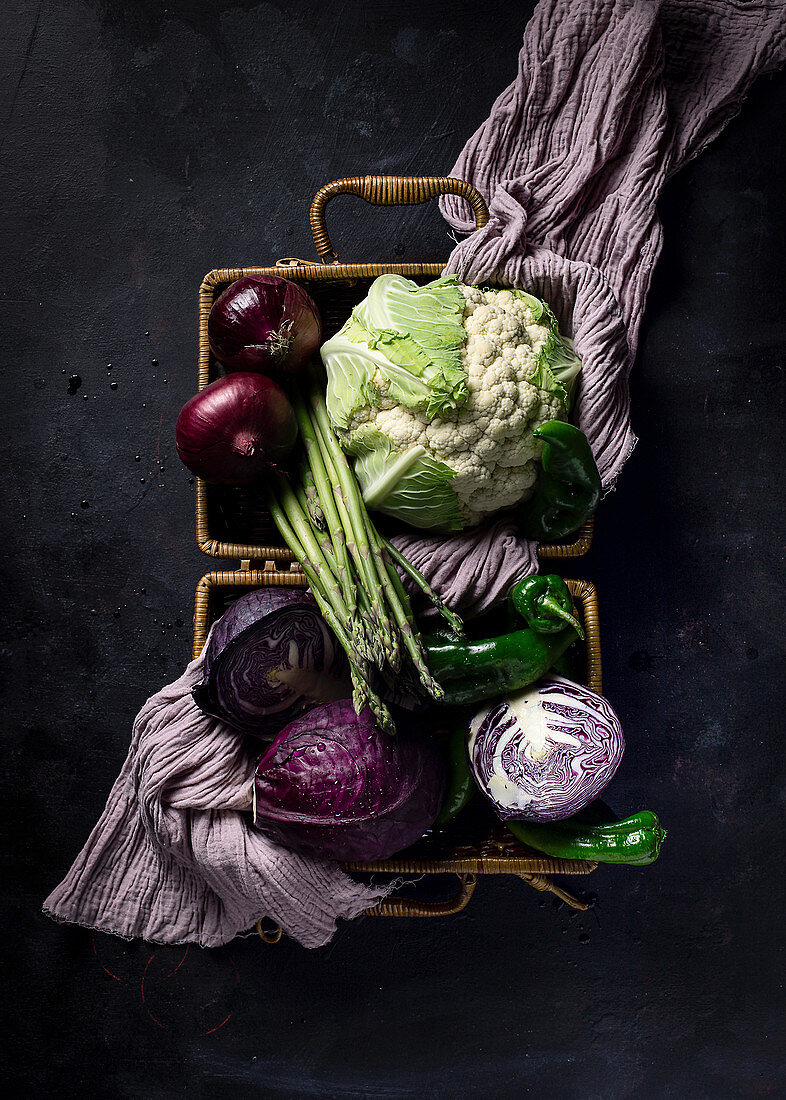 Verschiedene frische Gemüsesorten mit violettem Tuch im Weidenkorb