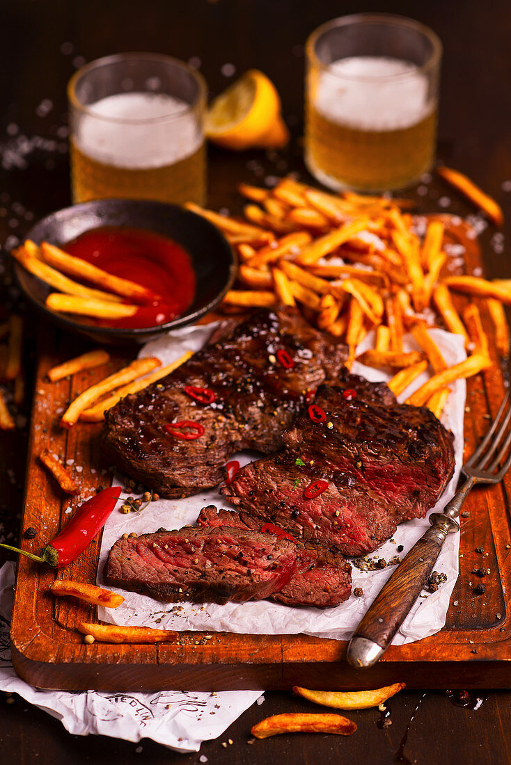 Beef steak in a sticky sauce with fries, ketchup and beer