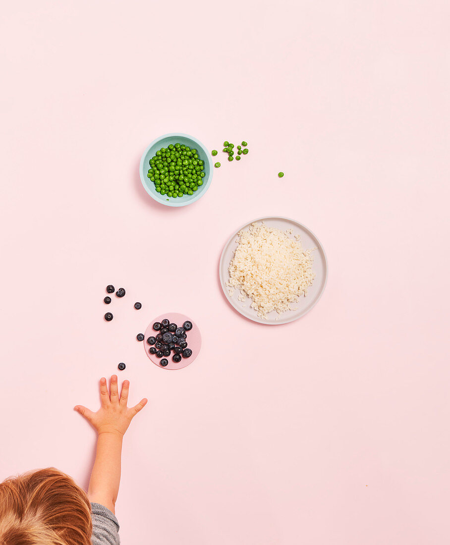 Kinderhände greifen nach Reis, Erbsen und Blaubeeren