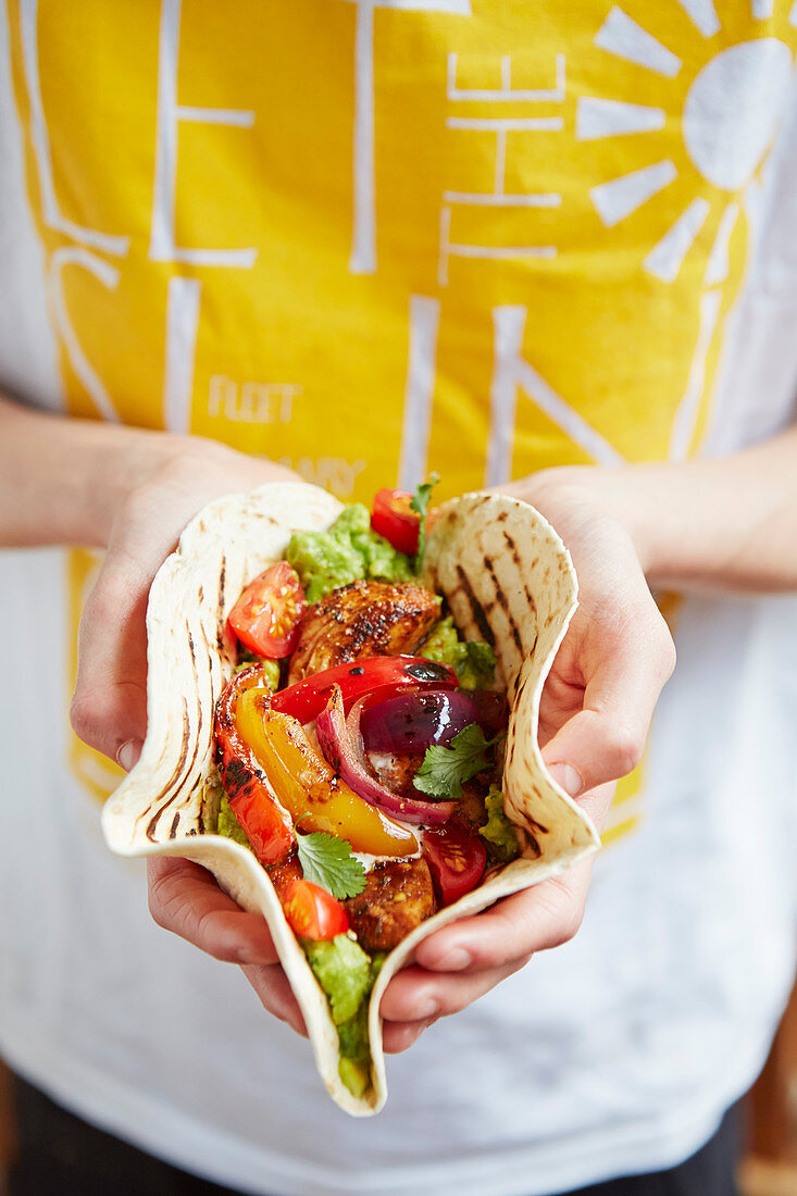 Hände halten Fajita mit Hähnchen und Tomaten