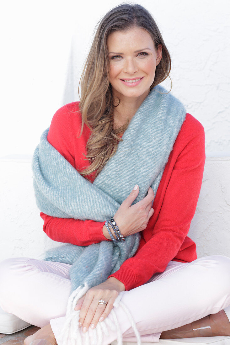 A young woman wearing a red jumper and white trousers with a shawl over her shoulders