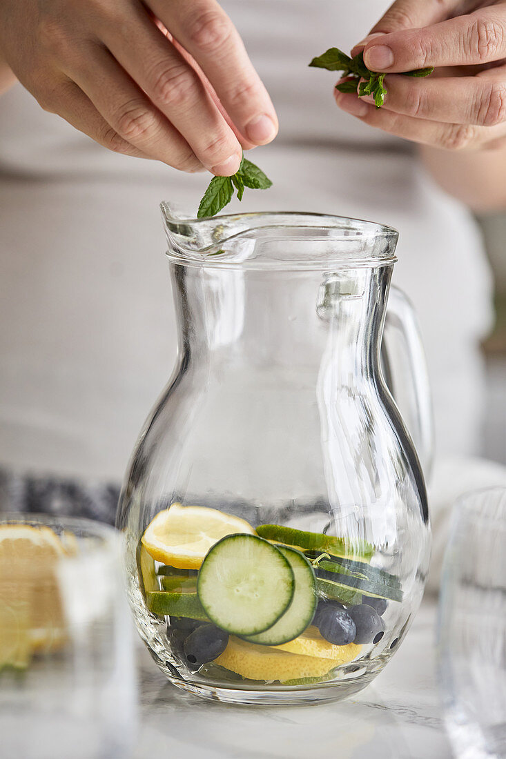 Adding mint leaves into a jug for cold infused water