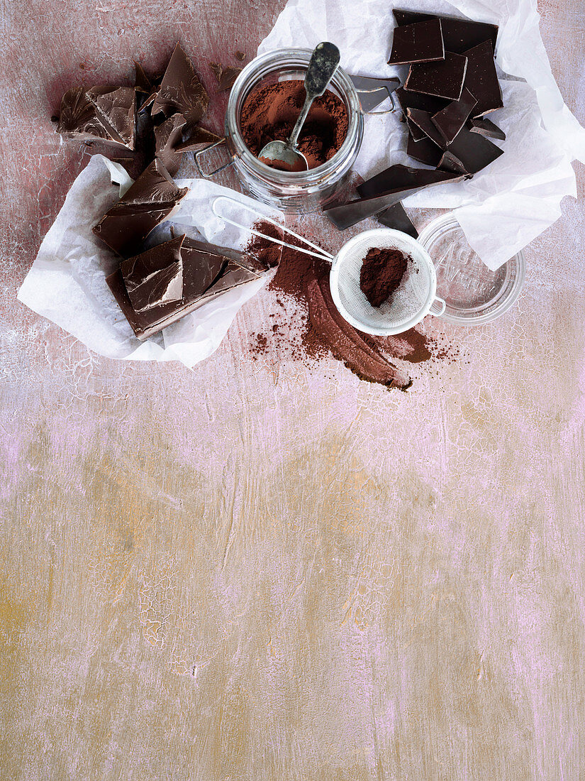 Kakaopulver in Glas und Küchensieb, dunkle Schokolade in Stücken