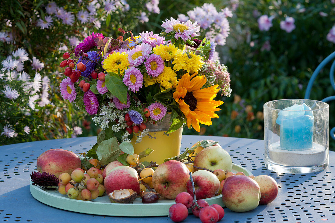 Colorful table setting with bouquets of chrysanthemums, summer asters, sunflower, hydrangea, sedum and crabapple, and apples on a tray