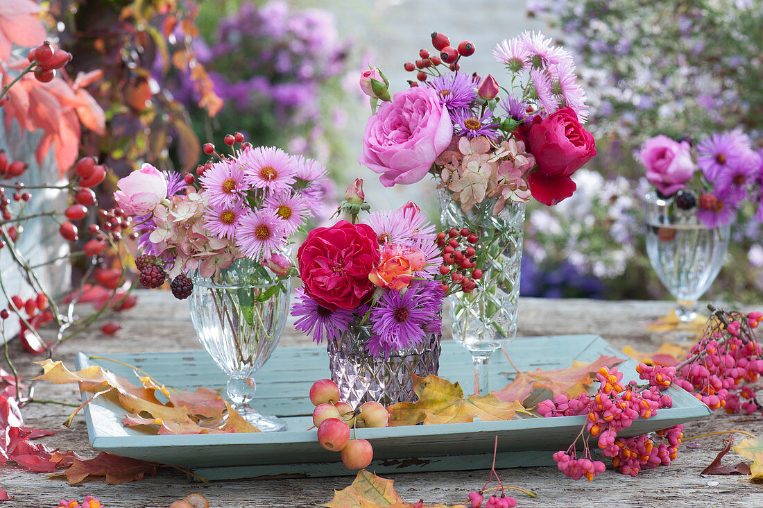 Small bouquets of roses, asters, rose hips, hydrangea and blackberry, common spindle, ornamental apples, and leaves on wooden bowls