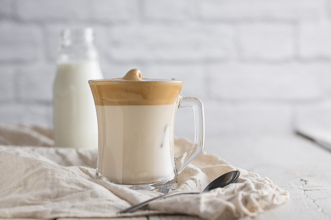 Cold homemade Dalgona beverage with whipped coffee placed on wooden table with bottle of milk and teaspoon