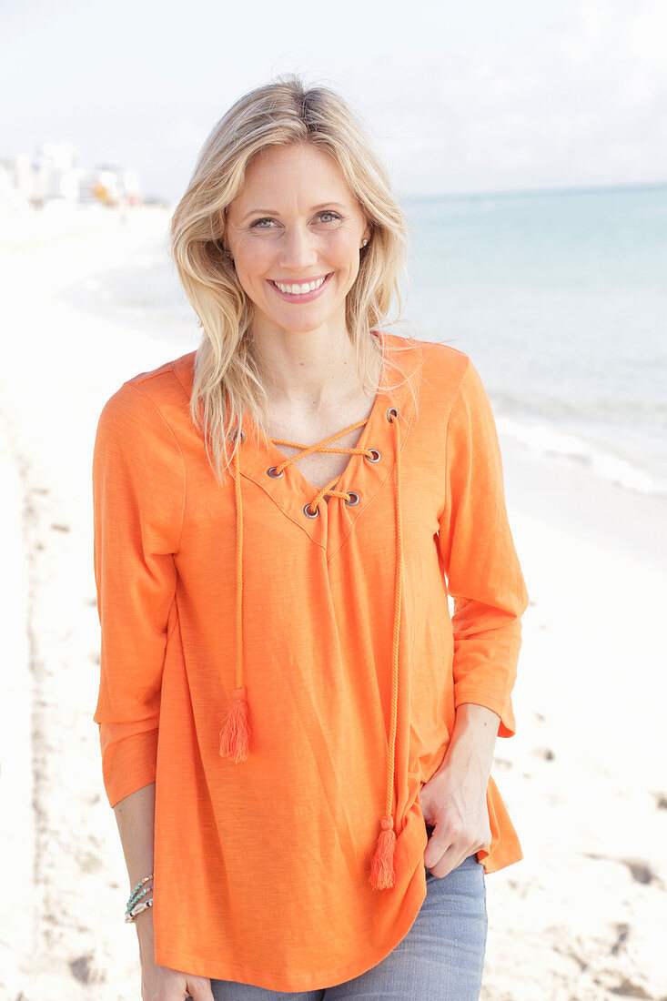 Blonde Frau in orangefarbener Tunikabluse am Meer