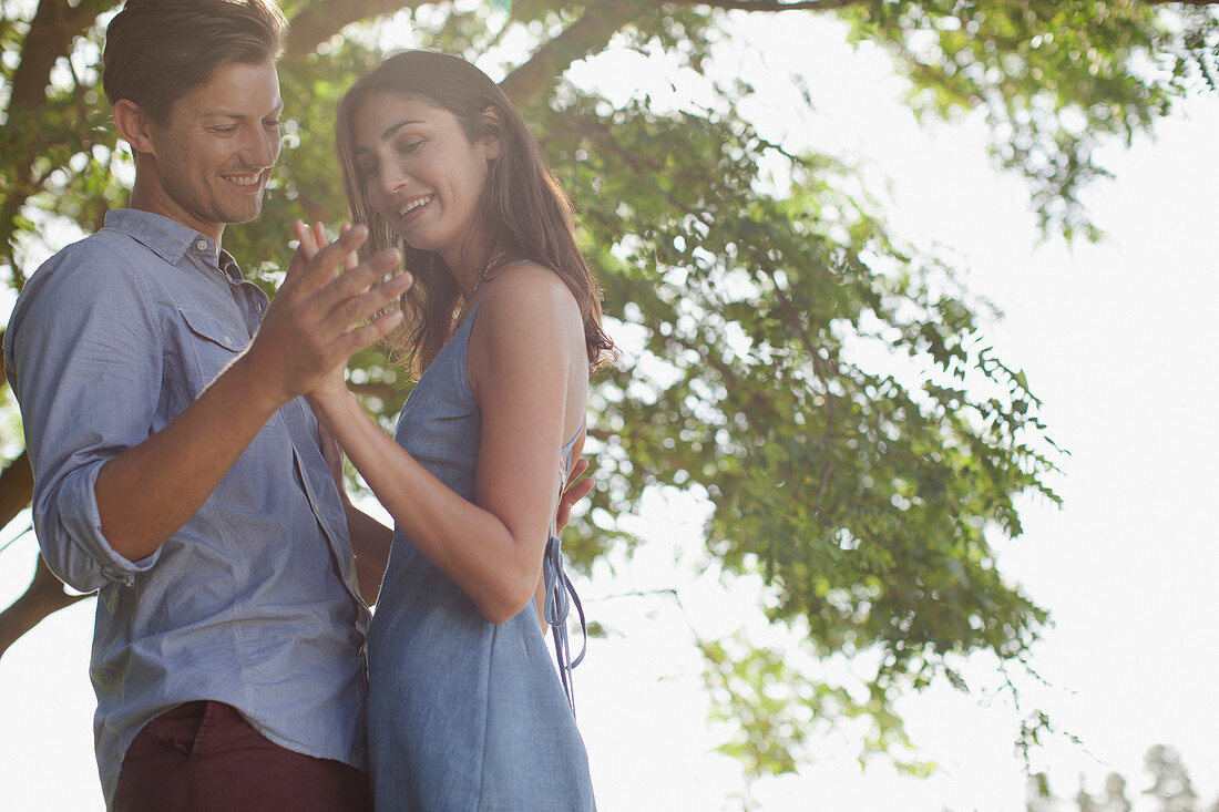 Smiling couple holding hands under tree