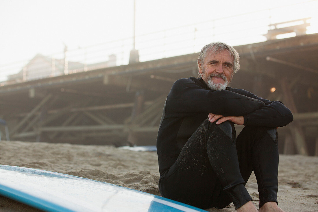 Older surfer sitting with board on beach