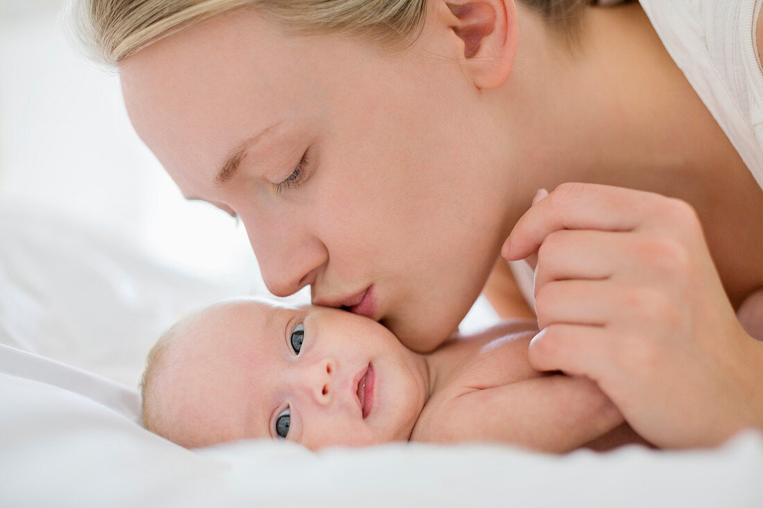 Mother kissing newborn baby on bed