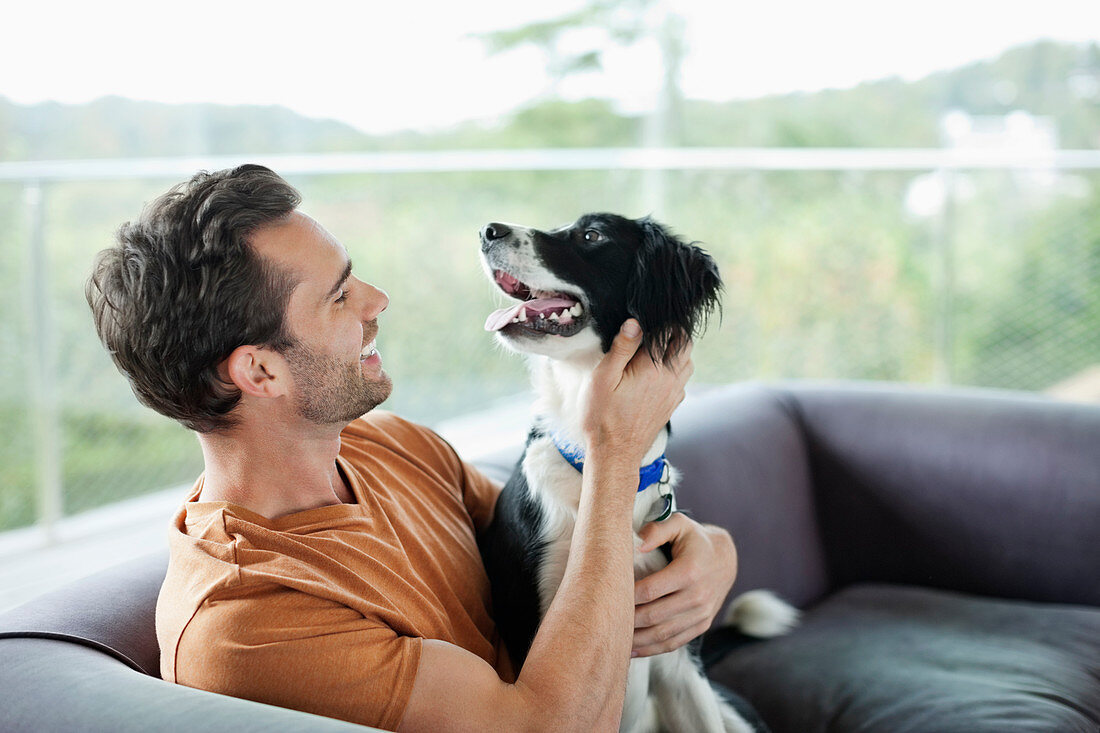 Smiling man petting dog on sofa