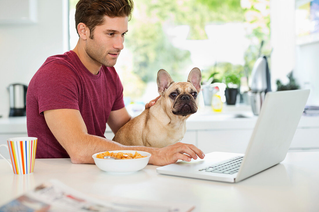 Man on laptop petting dog in kitchen