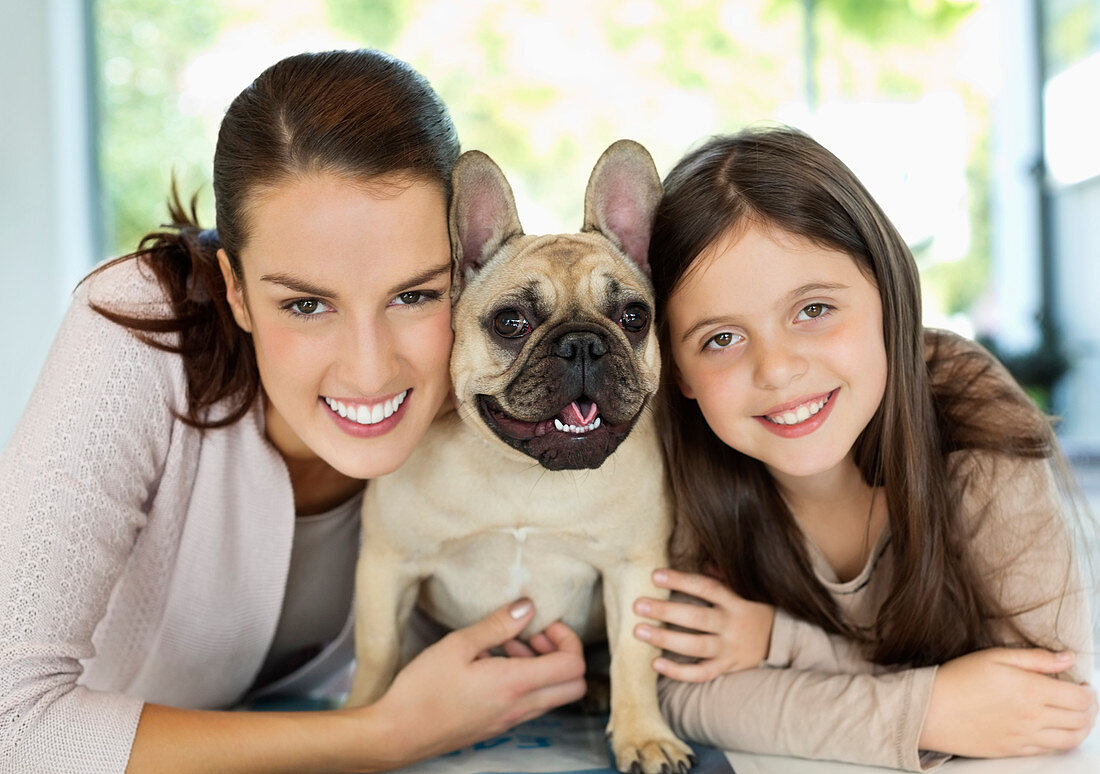 Smiling mother and daughter hugging dog