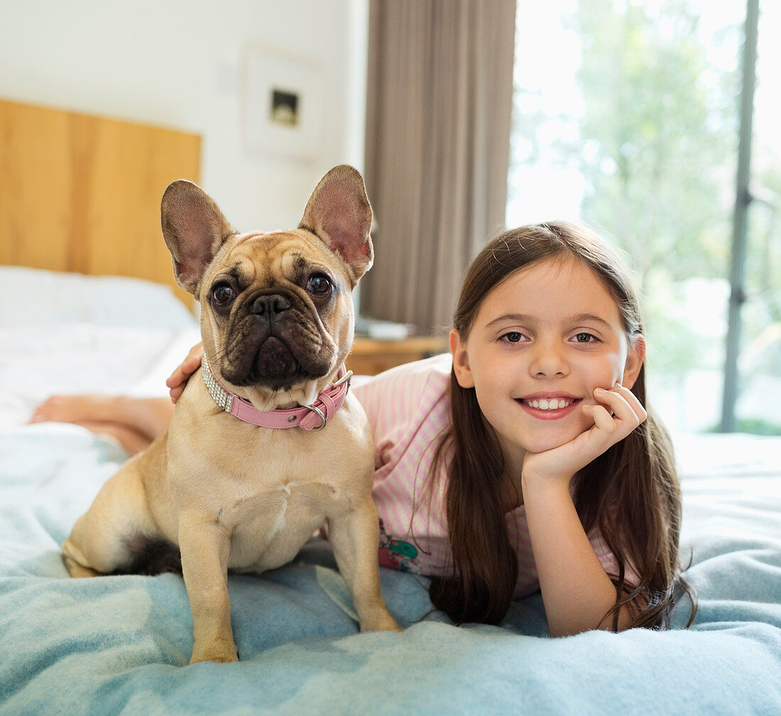 Smiling girl relaxing with dog on bed