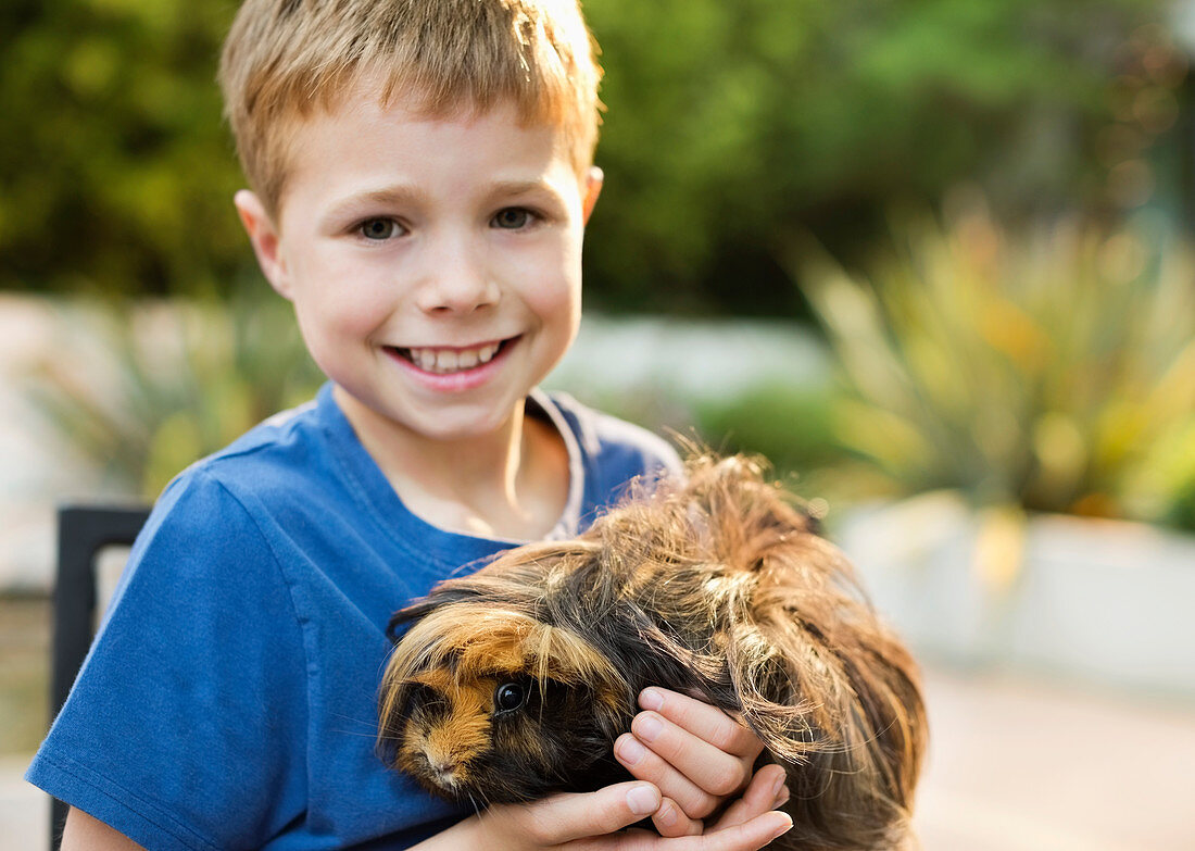 Smiling boy holding guinea pig outdoors