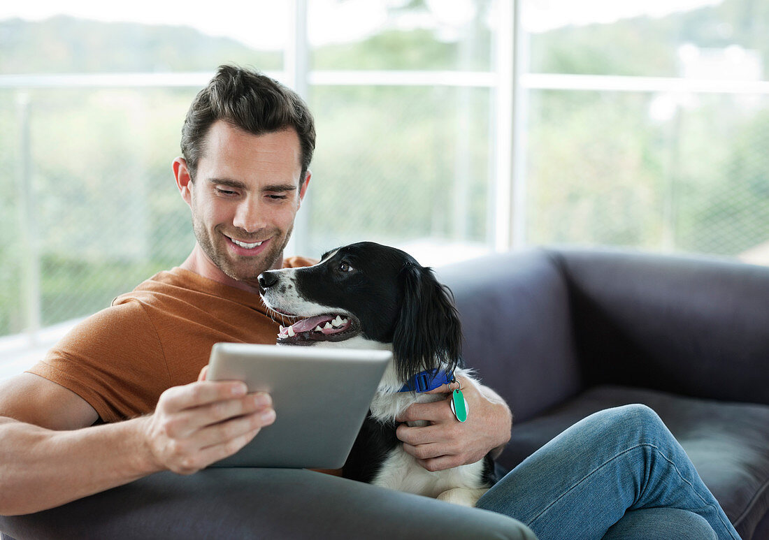 Man petting dog and using tablet computer