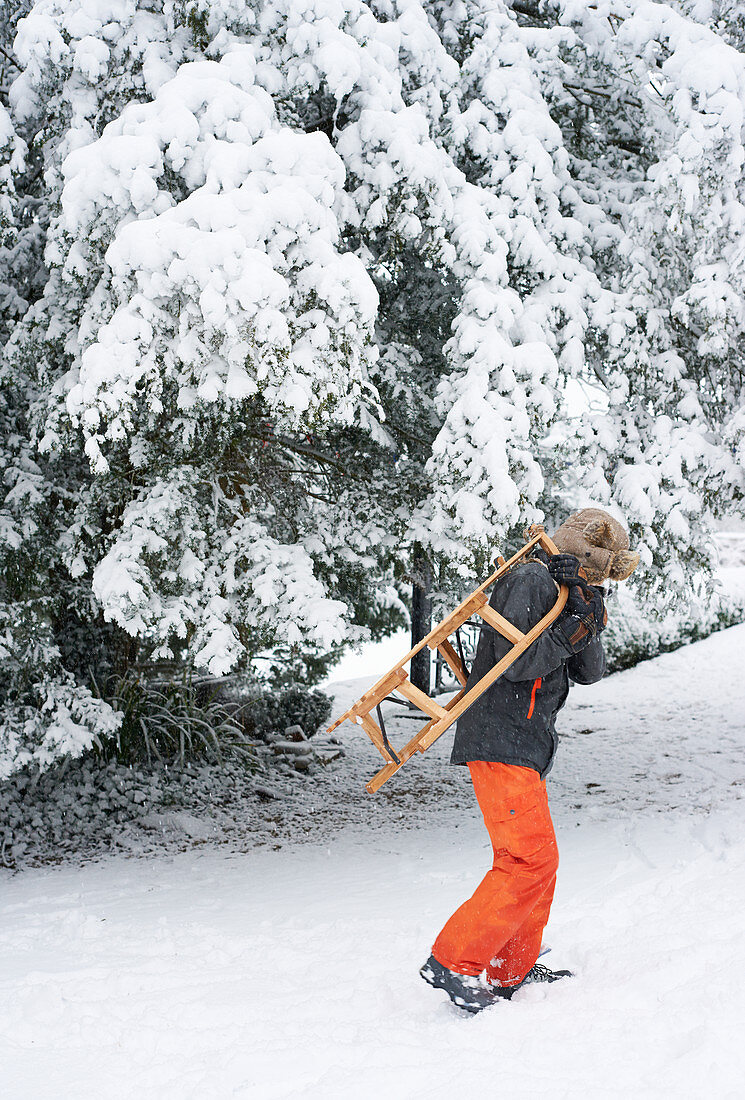 Boy carrying wooden sled in snow