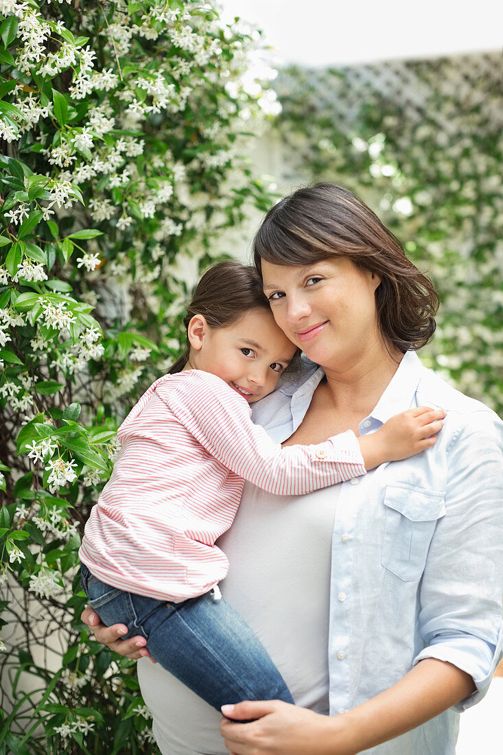 Pregnant mother holding daughter outdoors