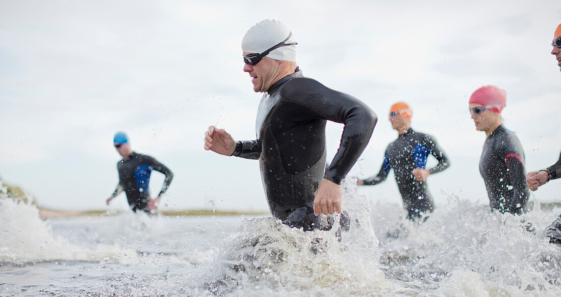 Triathletes in wetsuits running in waves