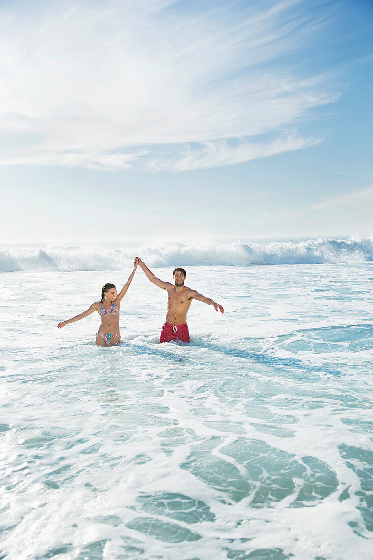 Couple standing in ocean with arms raised