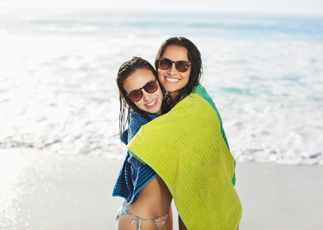 Smiling friends wrapped in towel on beach