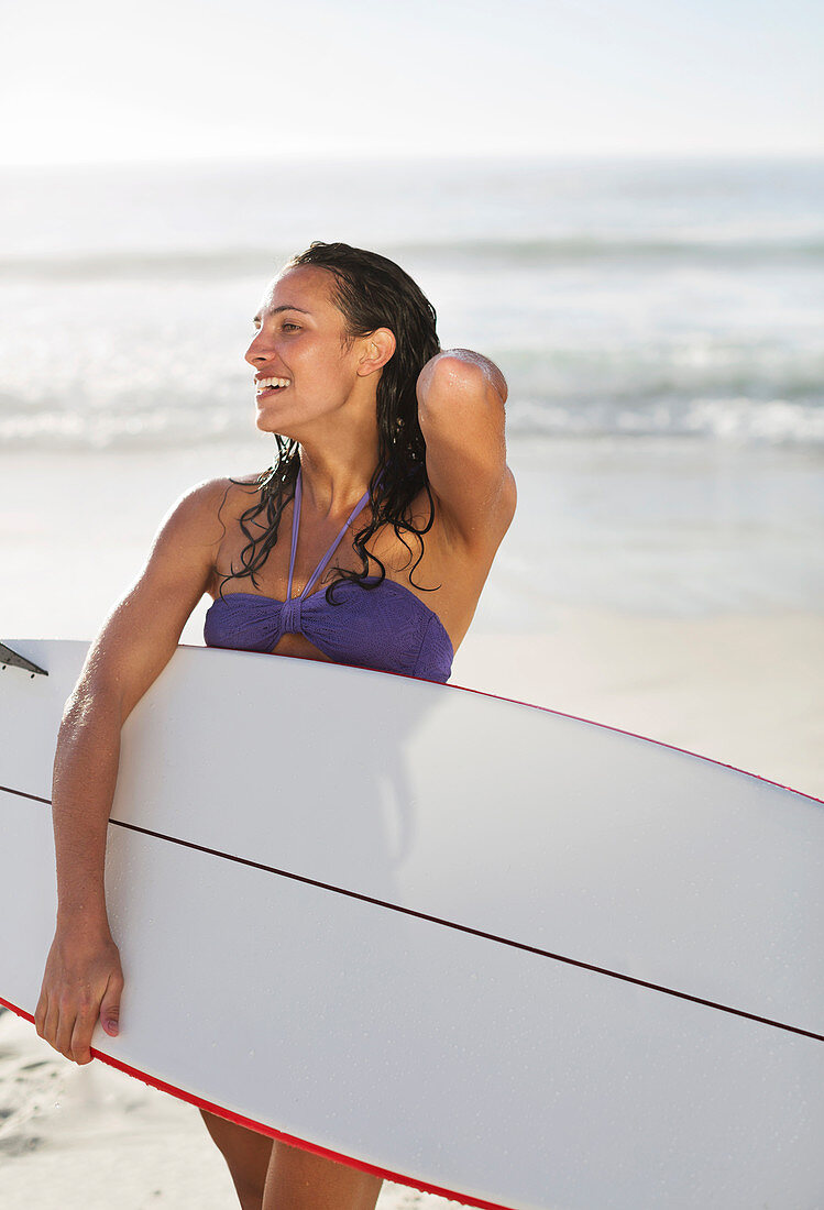 Smiling woman holding surfboard on beach