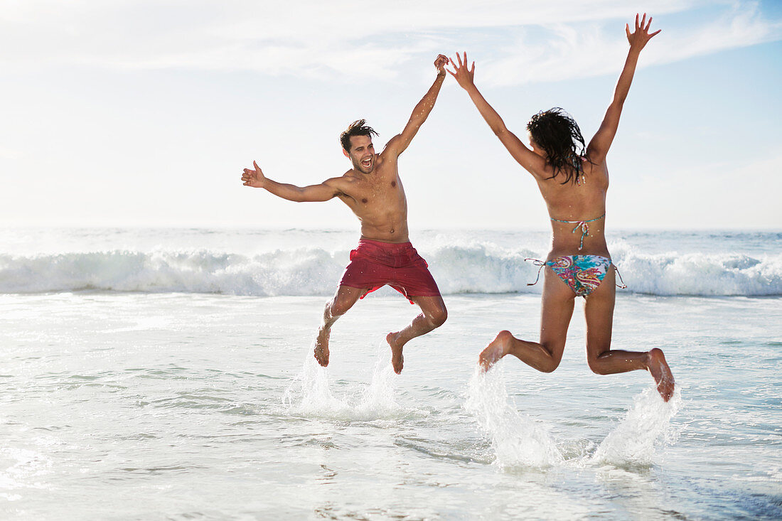 Couple jumping with arms raised on beach