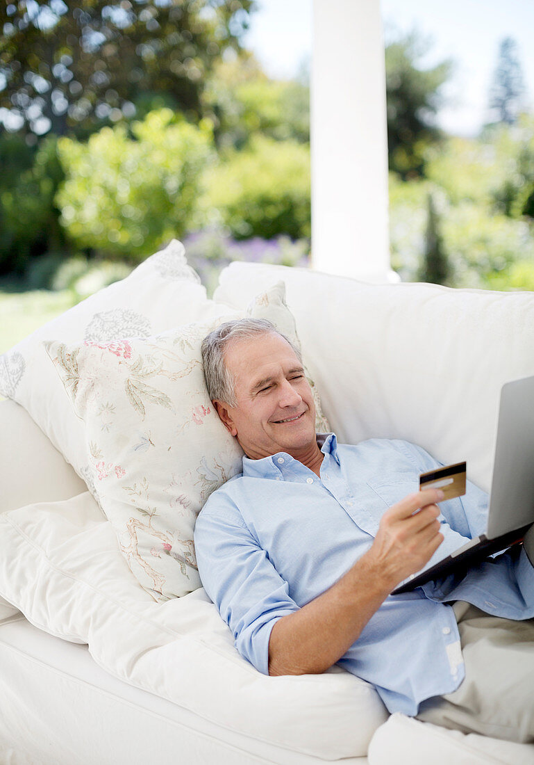 Senior man shopping online on patio sofa