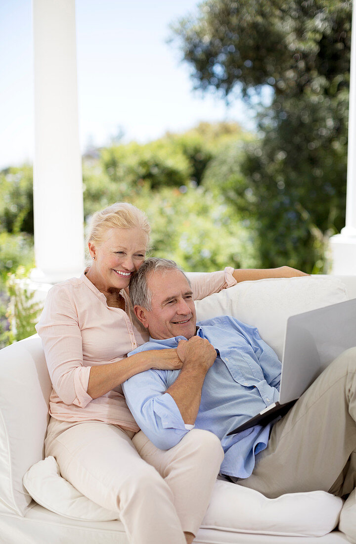 Senior couple using laptop on patio sofa