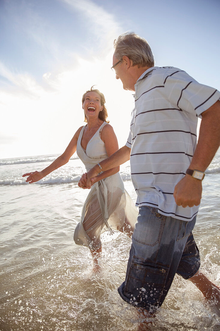 Older couple playing in waves on beach