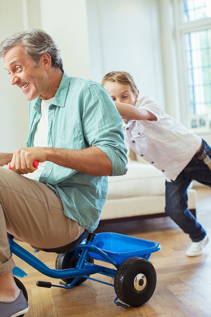 Boy pushing father on tricycle indoors
