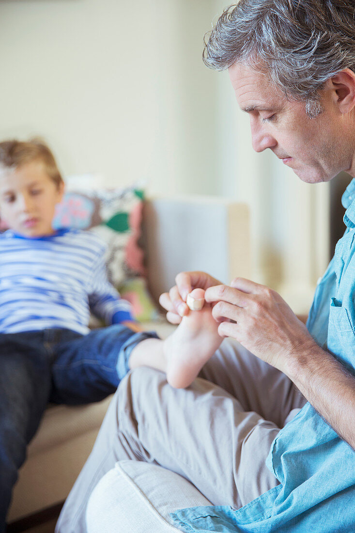 Father bandaging son's toe