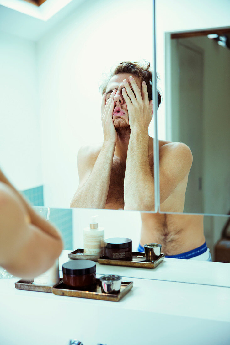 Hungover man covering face at mirror