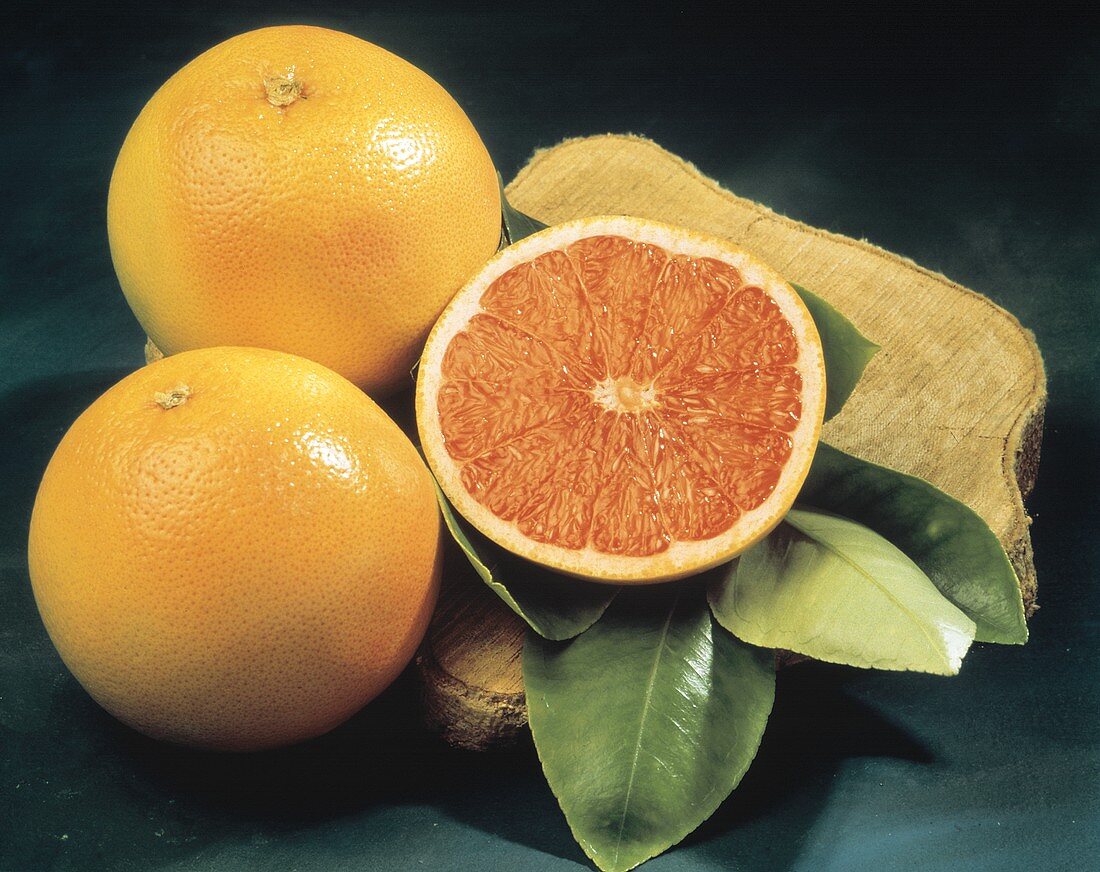 Zwei ganze & eine halbe Grapefruit mit Blättern auf Holzbrett