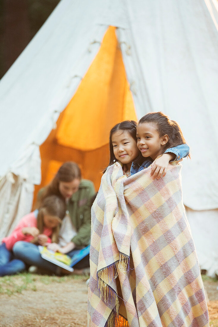 Girls wrapped in blanket at campsite