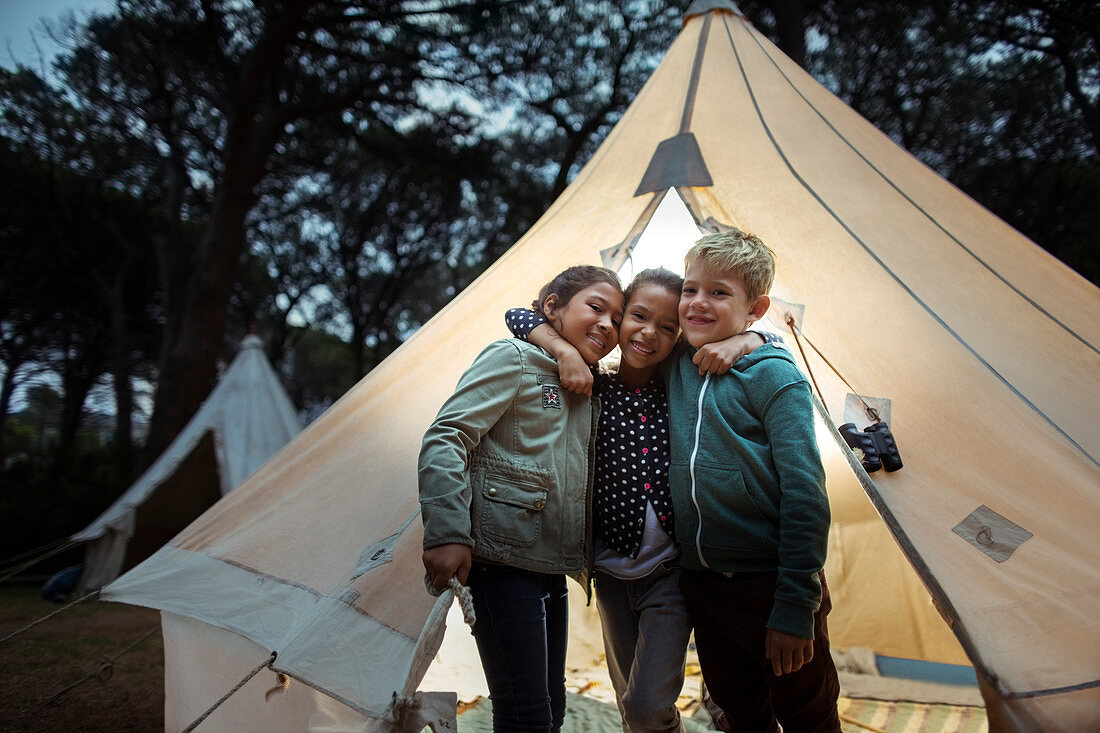 Children hugging by teepee at campsite