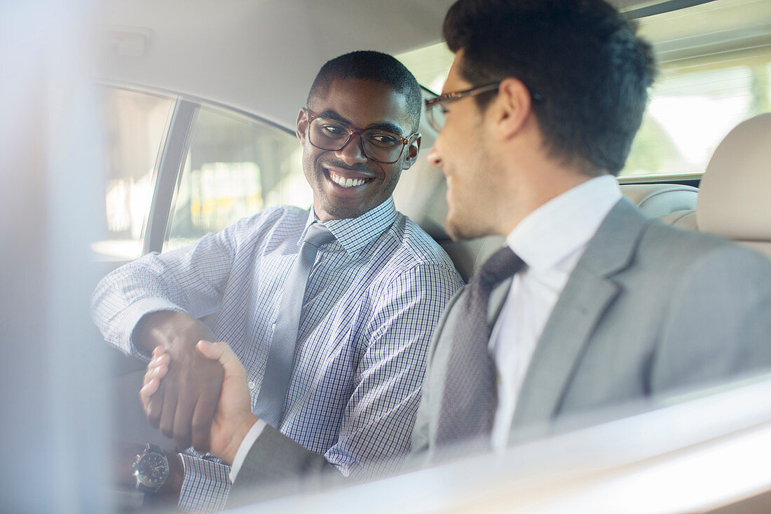 Smiling businessmen shaking hands in car