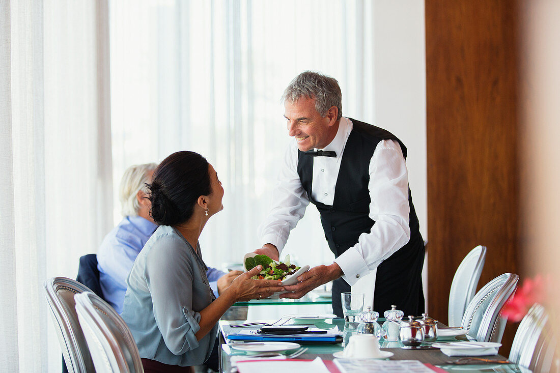 Smiling waiter serving salad