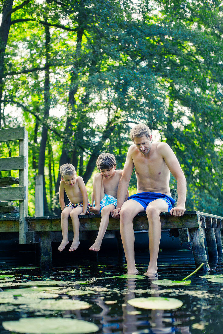 Father and sons dangling feet in lake