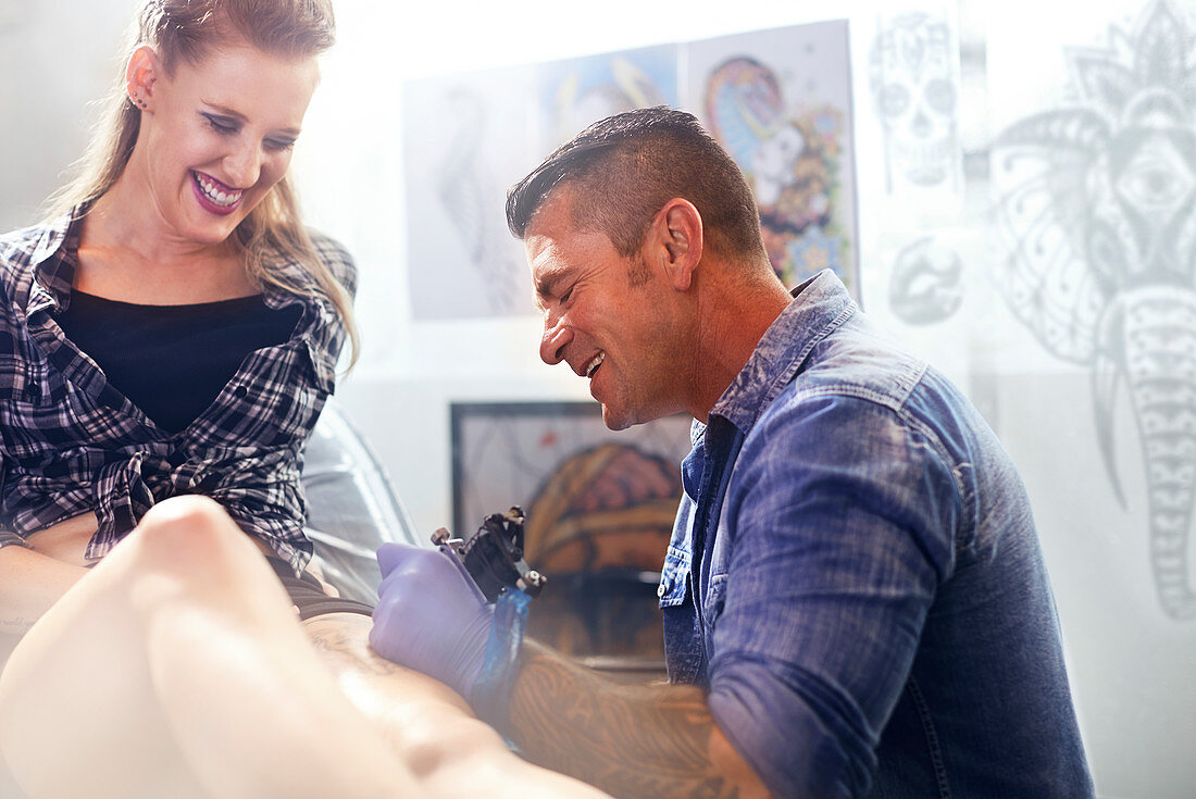 Tattoo artist tattooing woman's thigh