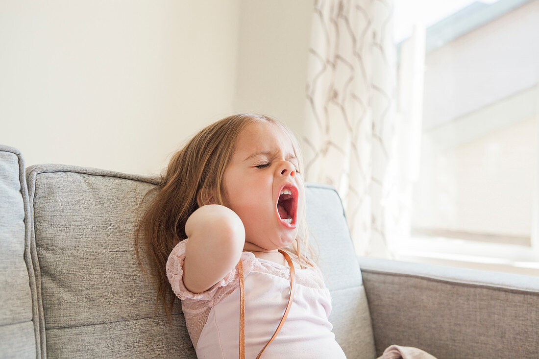 Toddler girl yawning on sofa