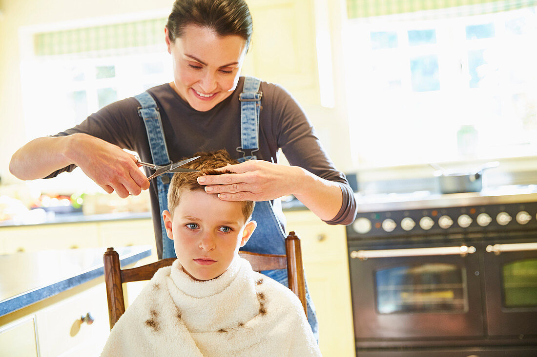 Unhappy boy getting haircut from mother