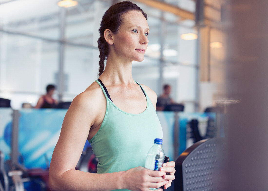 Pensive woman drinking water at gym