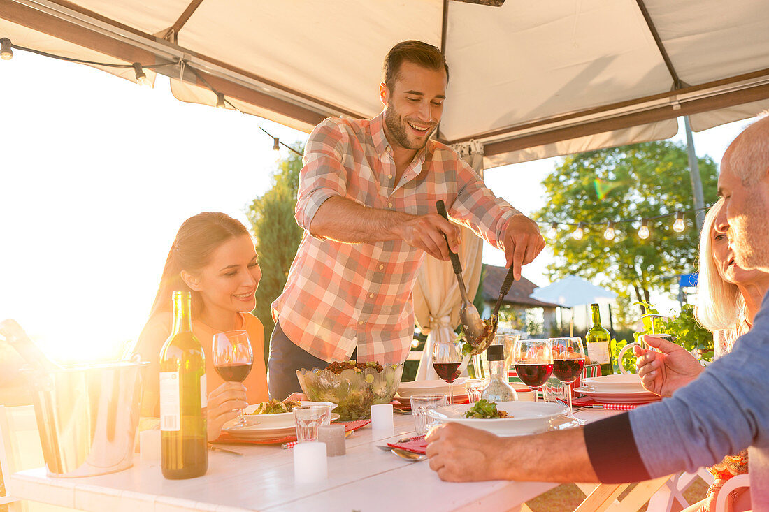 Man serving salad at sunny patio table