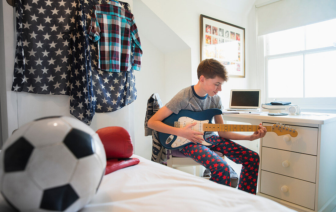 Boy playing electric guitar in bedroom